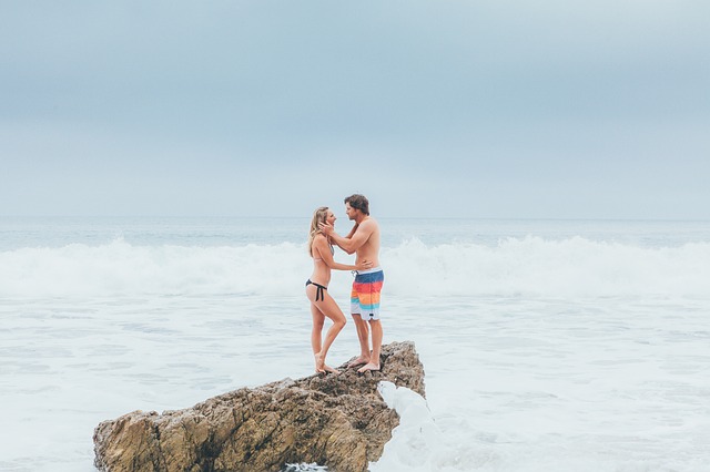 Muž drží ženu za tvár a stoja na skale v mori.jpg