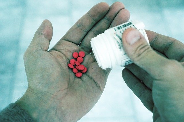 Muž drží v ruke obal od liekov a na dlani má ružové tabletky.jpg