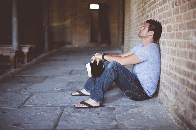 Muž s knihou sedí opretý o stenu 
